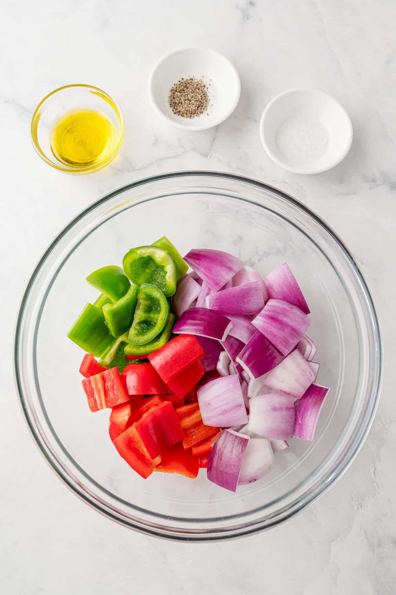 Bell peppers and onions in a bowl, with olive, salt, and pepper also visible. 