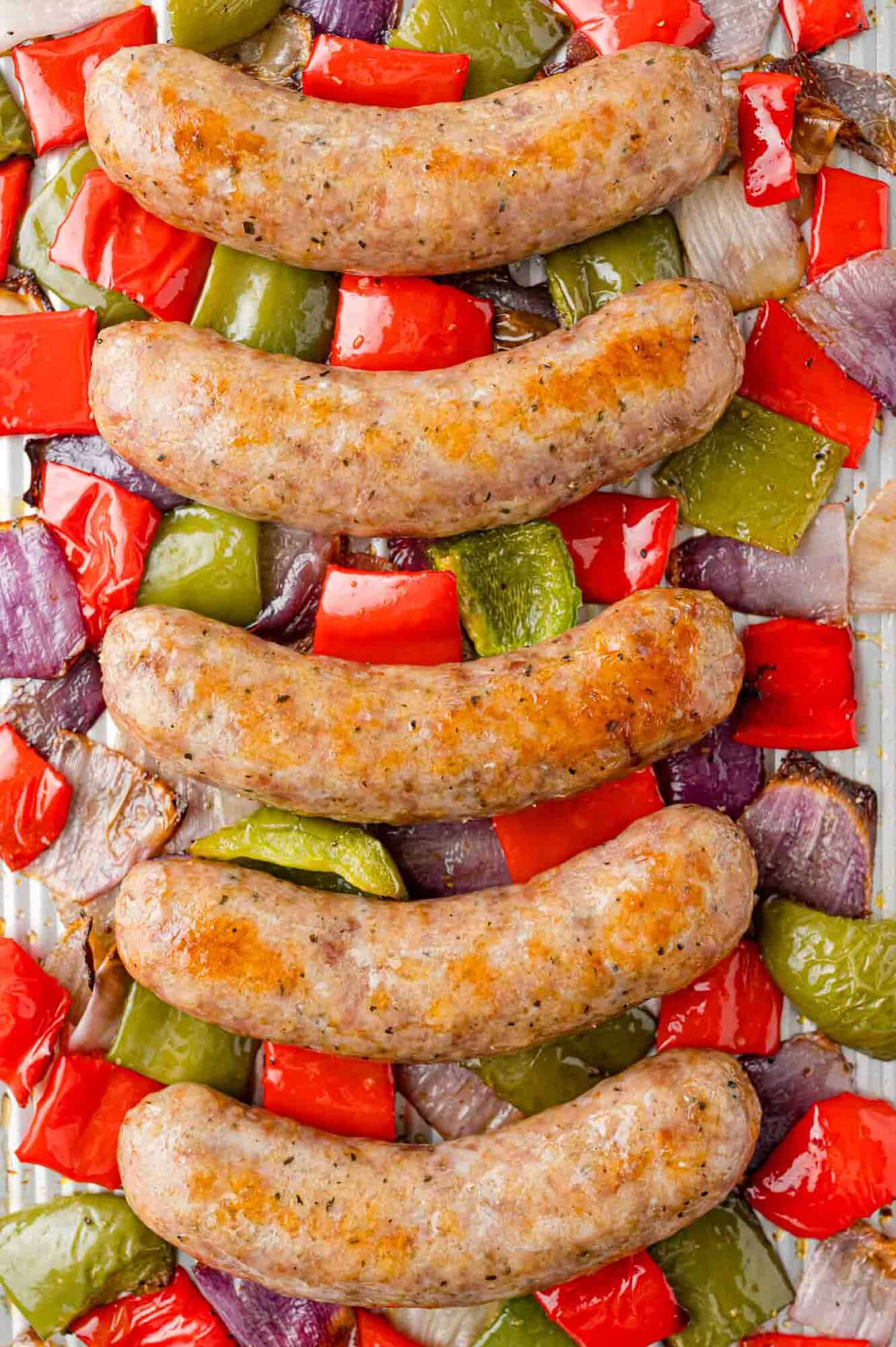 Cooked Italian sausage, bell peppers, and onions on a sheet pan.