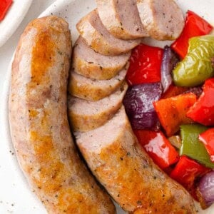 Baked Italian sausage with peppers and onions, on a plate, sausage partially sliced.