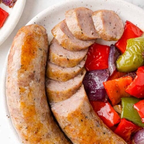 Baked Italian sausage with peppers and onions, partially sliced.