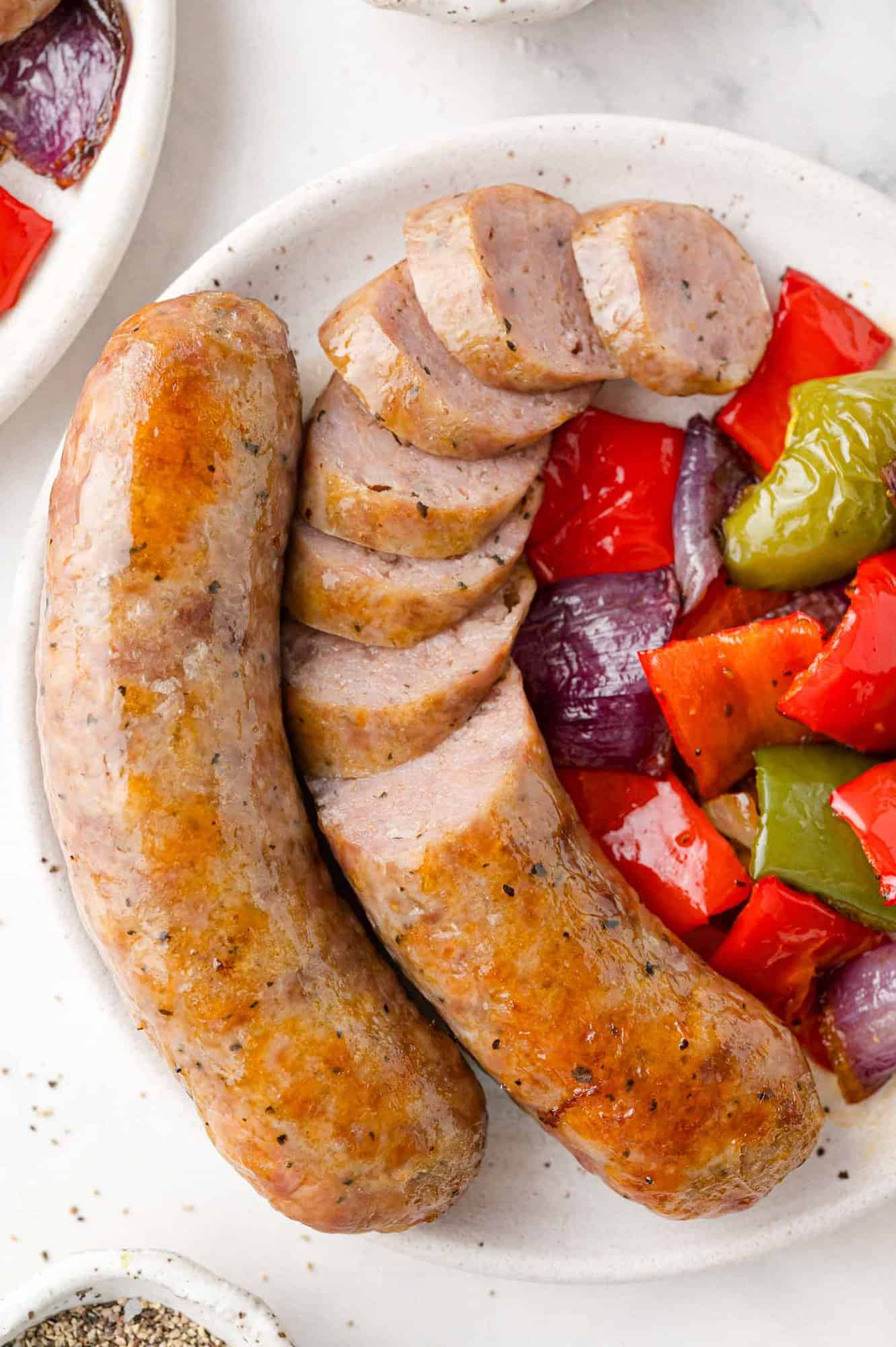 Baked Italian sausage with peppers and onions, on a plate, sausage partially sliced.