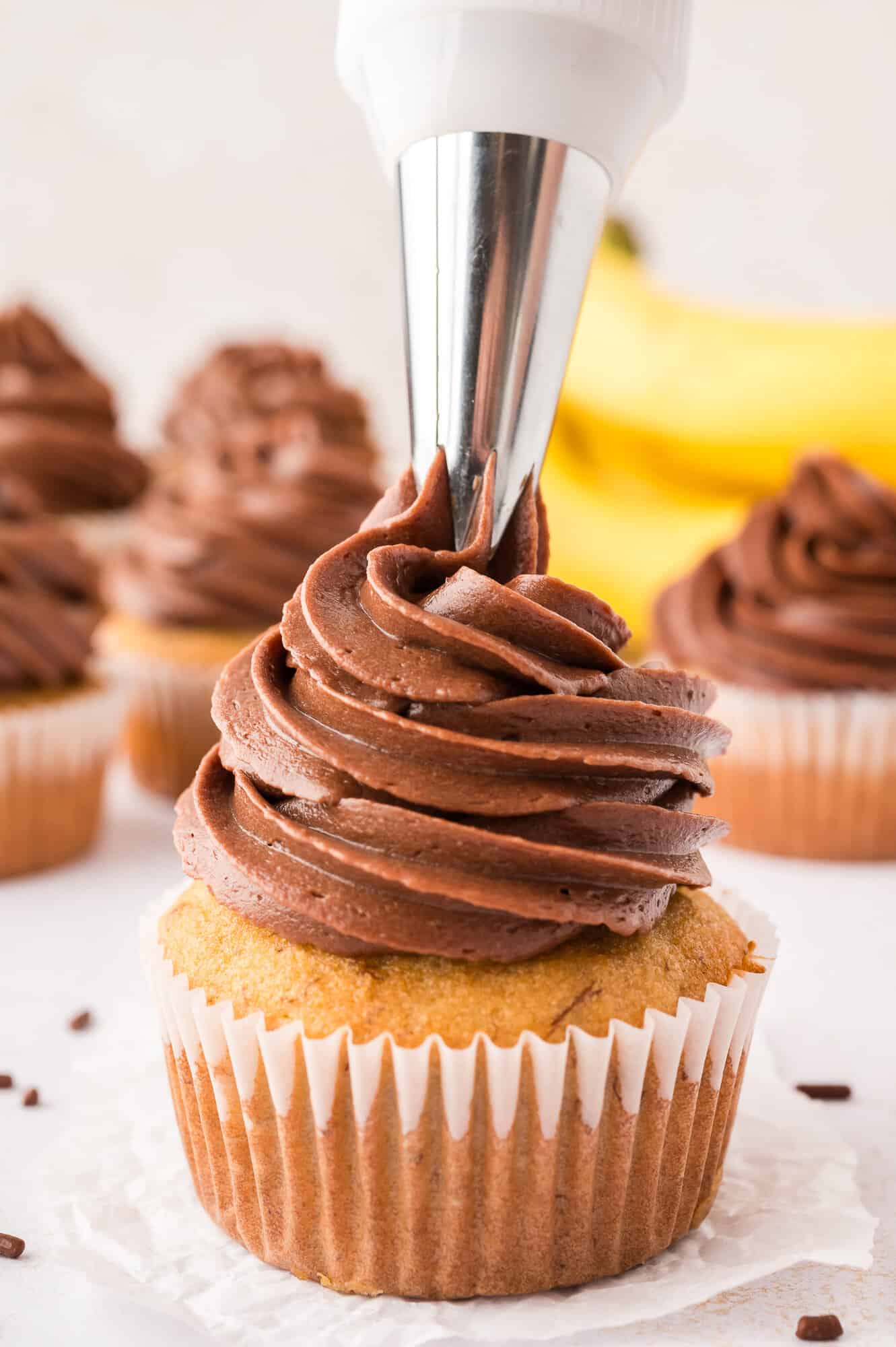Chocolate frosting being piped onto a banana cupcake.