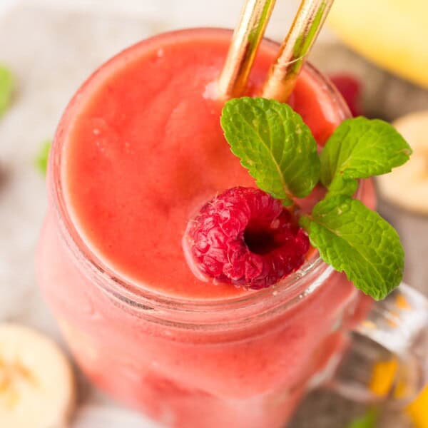 Overhead view of coconut water smoothie topped with raspberries and mint leaves.