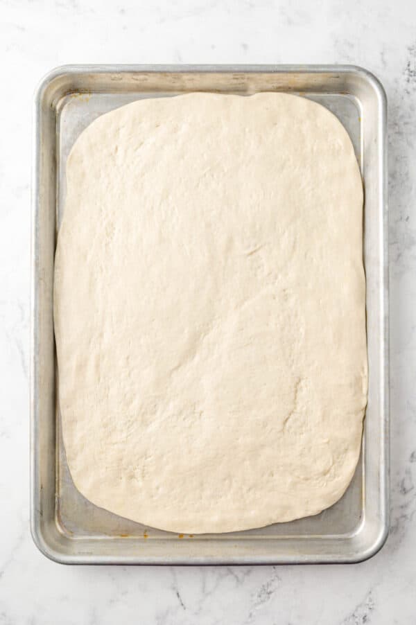 Pizza dough spread into sheet pan.