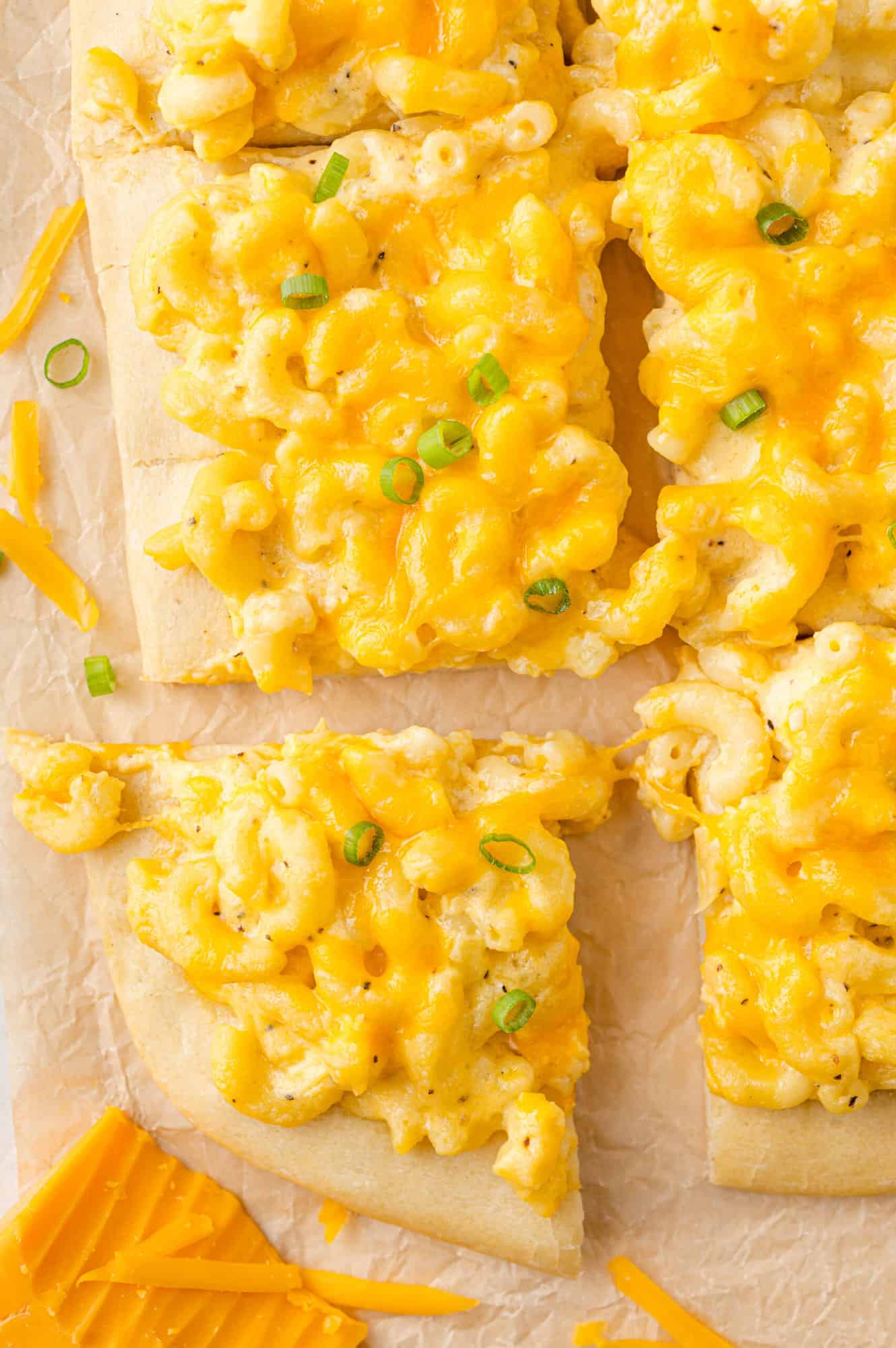 Mac and cheese pizza, topped with green onions and cut into squares.