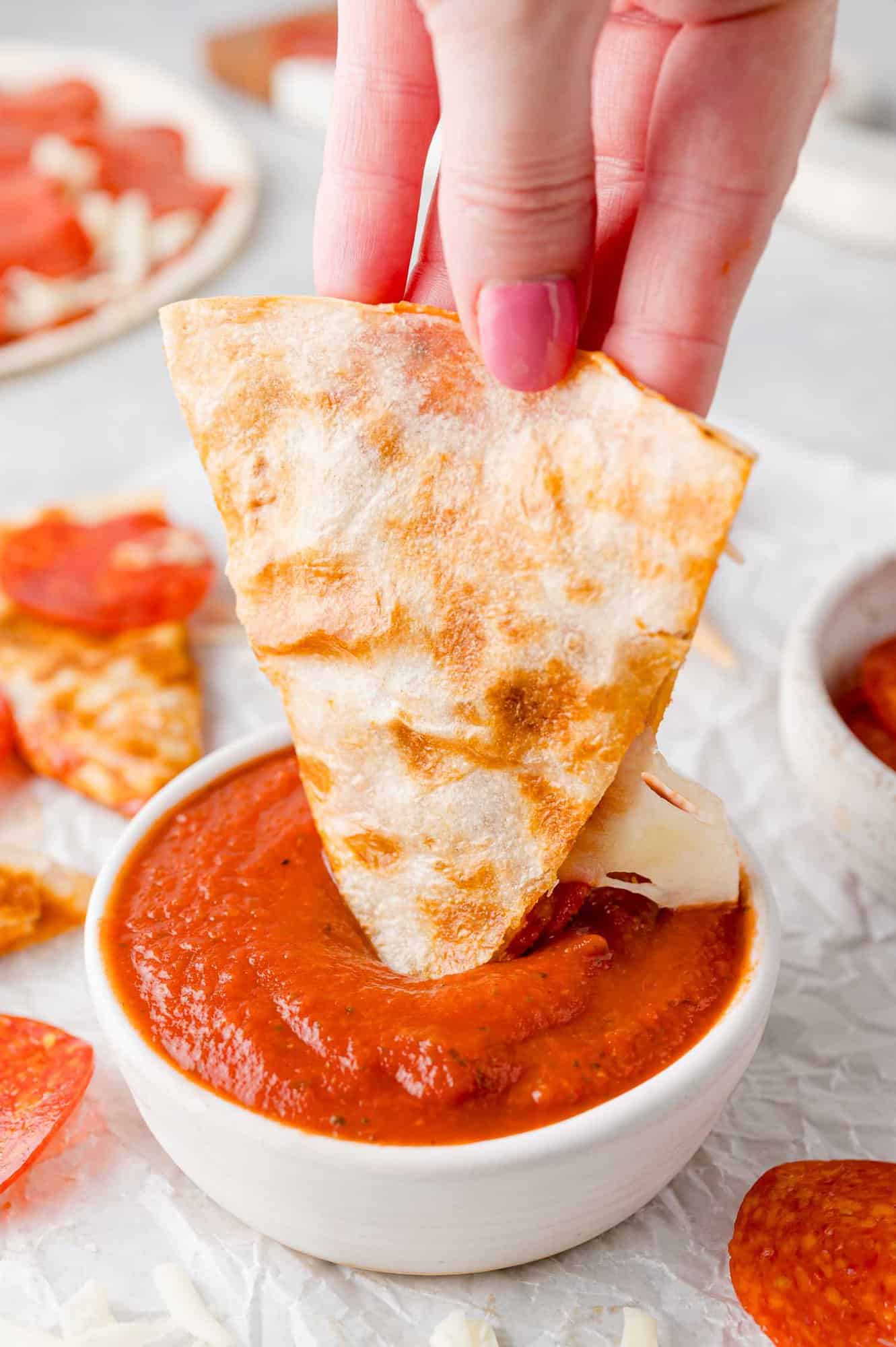 Pizza quesadilla being dipped into pizza sauce. 