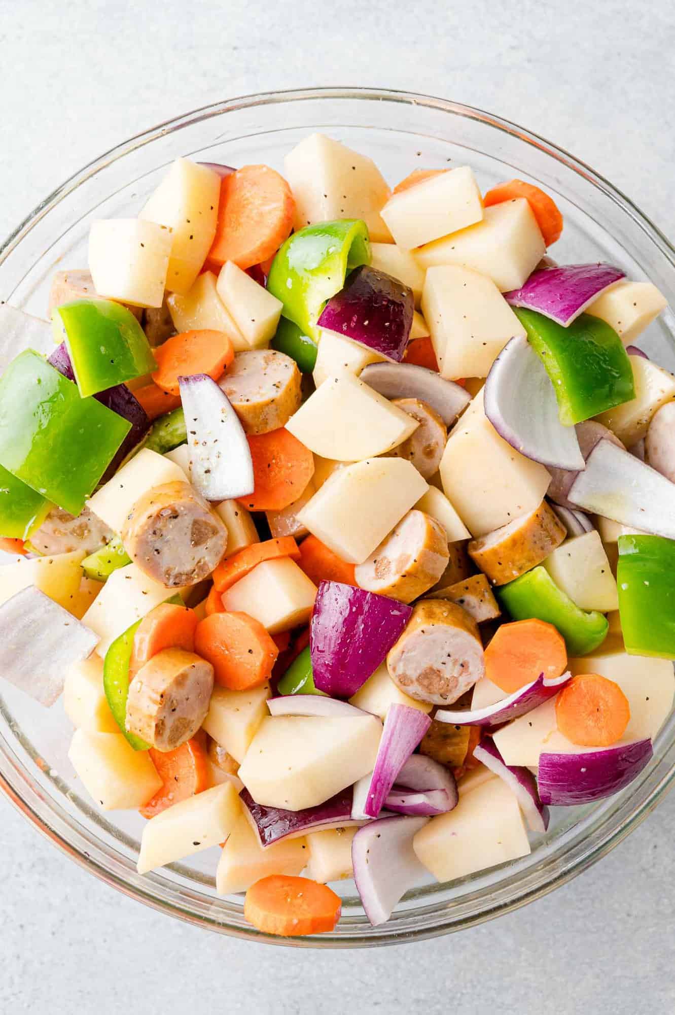 Sliced chicken sausage mixed with uncooked vegetables and potatoes.