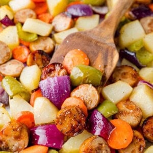 Sausage sheet pan dinner with sliced sausages, potatoes, and onions on a sheet pan with spatula.