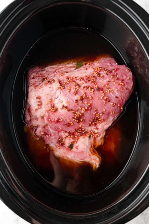Uncooked corned beef in a slow cooker with broth and seasonings.
