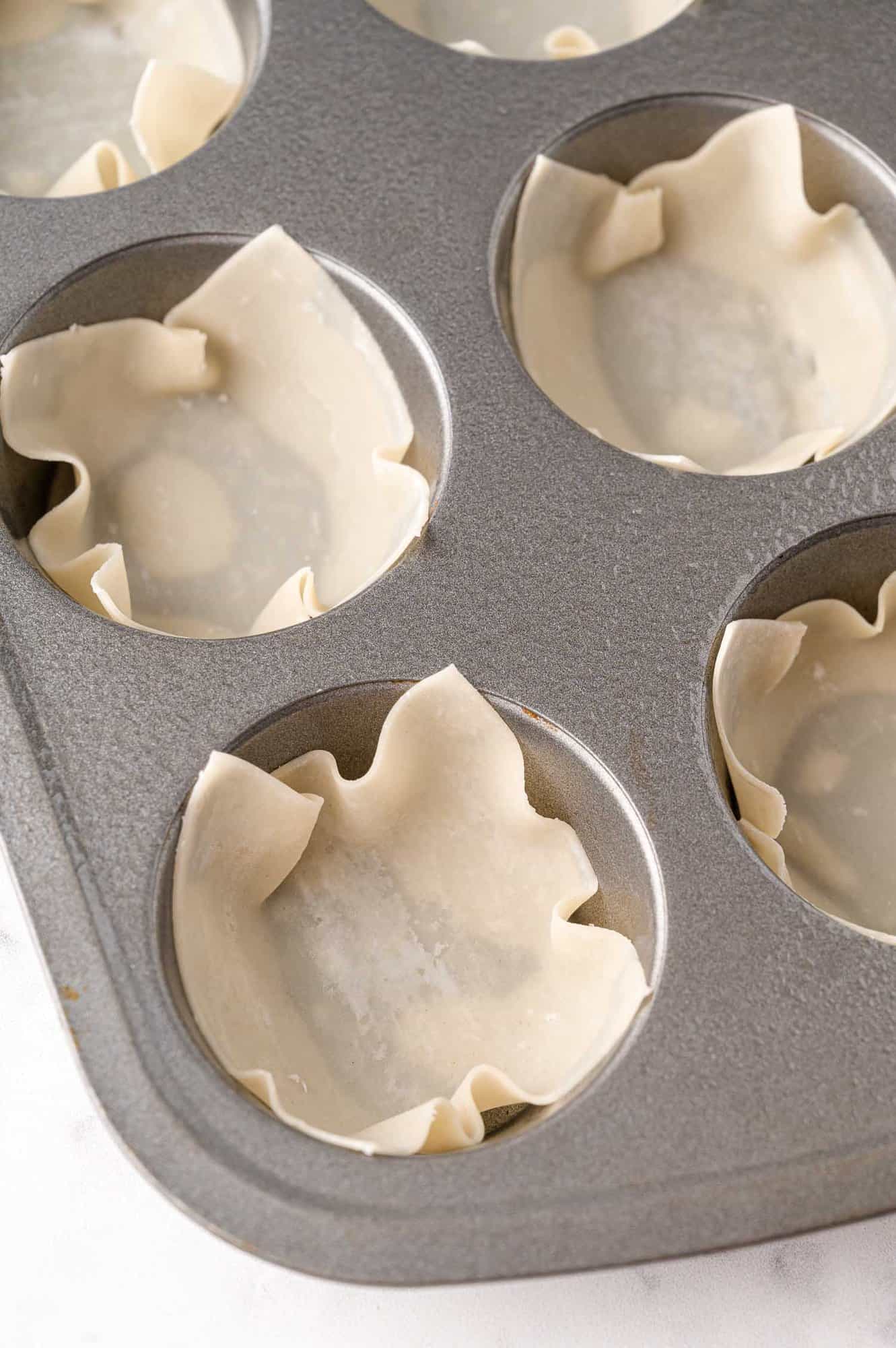 Wonton wrappers pressed into a muffin tin.