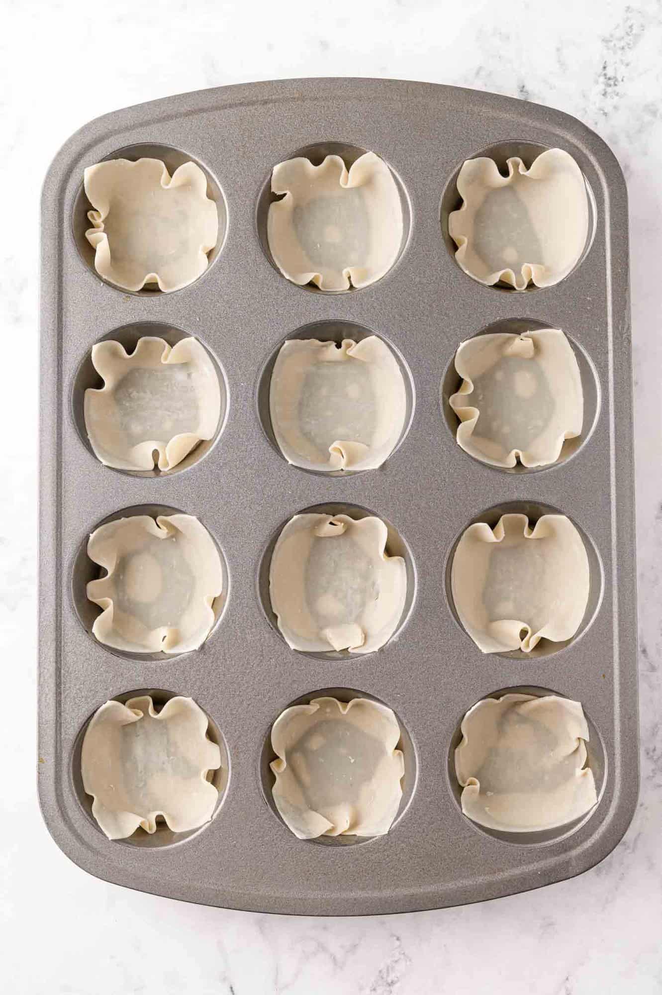 Wonton wrappers pressed into a muffin tin.