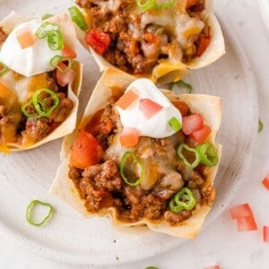 Overhead view of taco cups with sour cream and green onions.