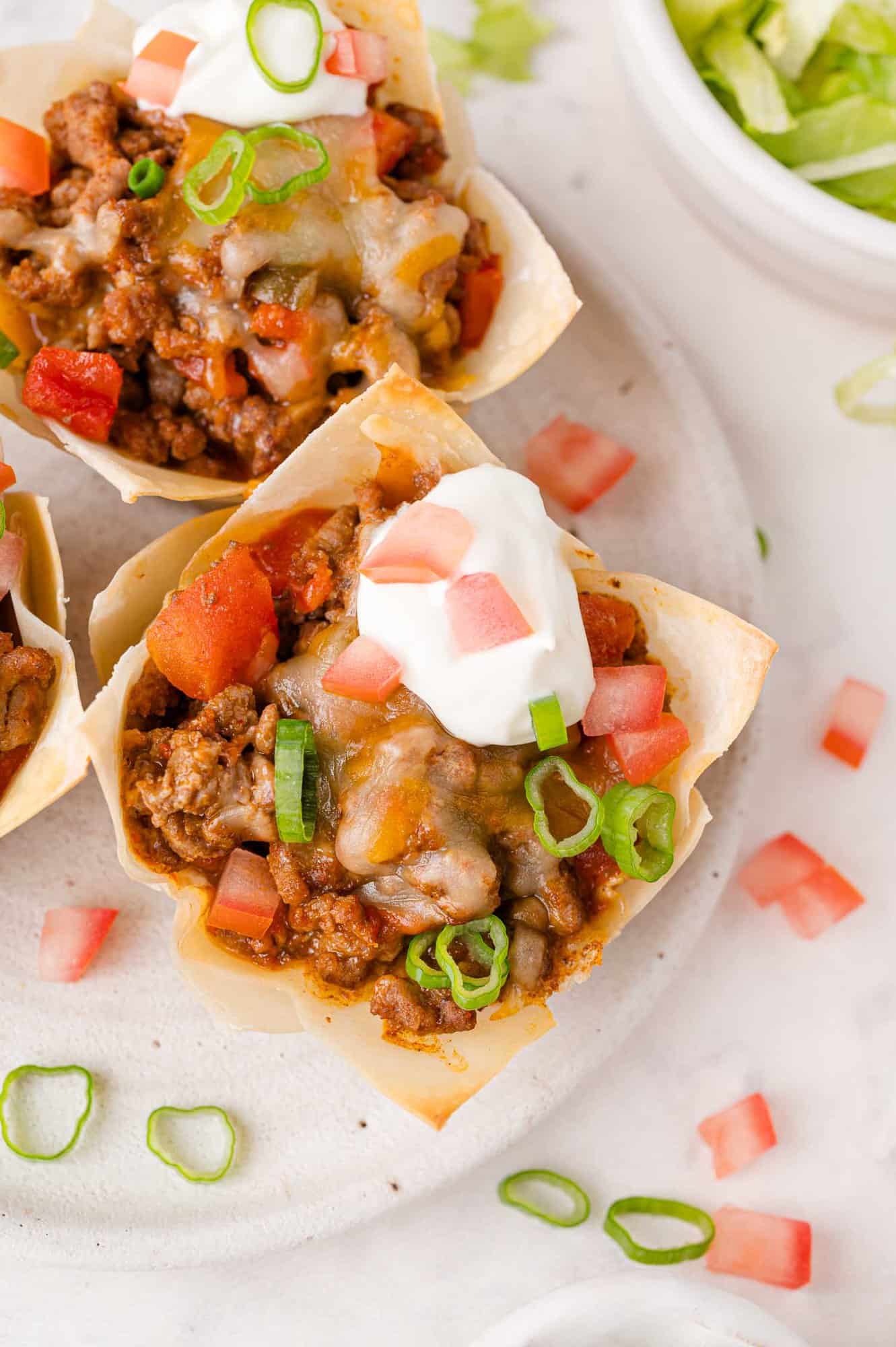 Overhead view of wonton taco cup, topped with sour cream and green onions.