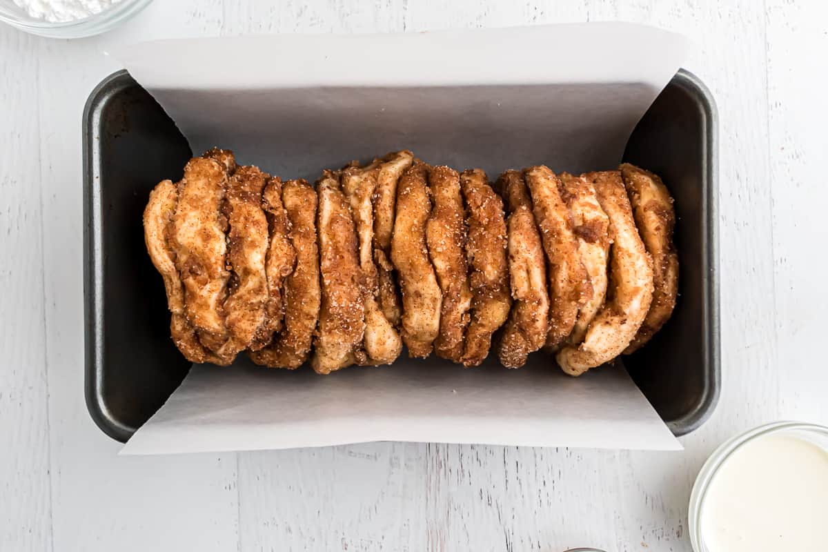 Cinnamon sugar coated biscuit pieces in parchment paper lined loaf pan.