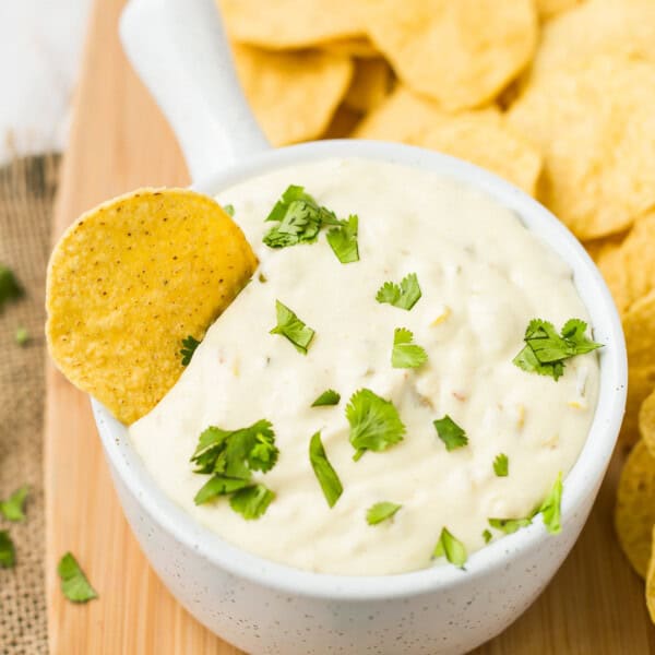 Queso blanco in a white bowl with handle, a chip dipped in.
