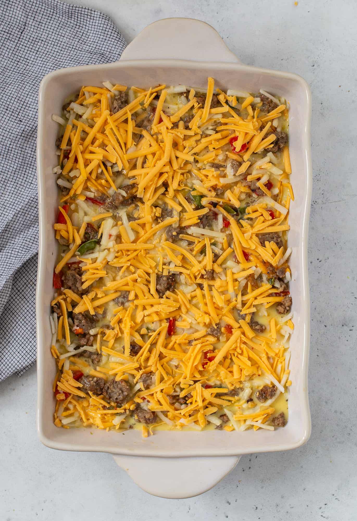 Shredded cheddar cheese added to the top of the unbaked casserole.