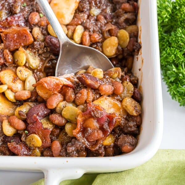 Calico beans in a white baking dish with a serving spoon.
