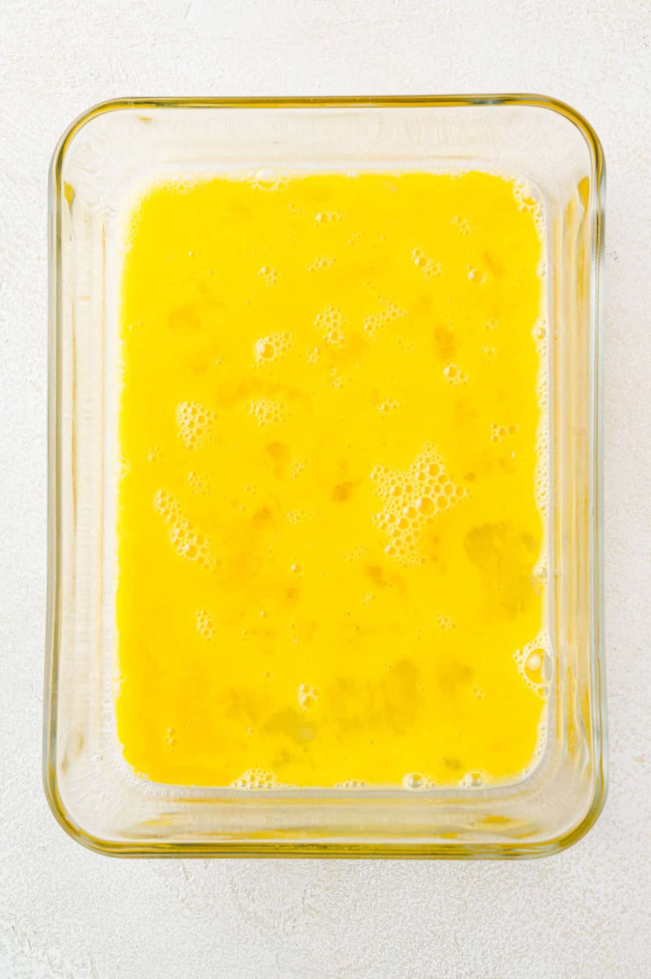 Beaten eggs in a square baking dish.