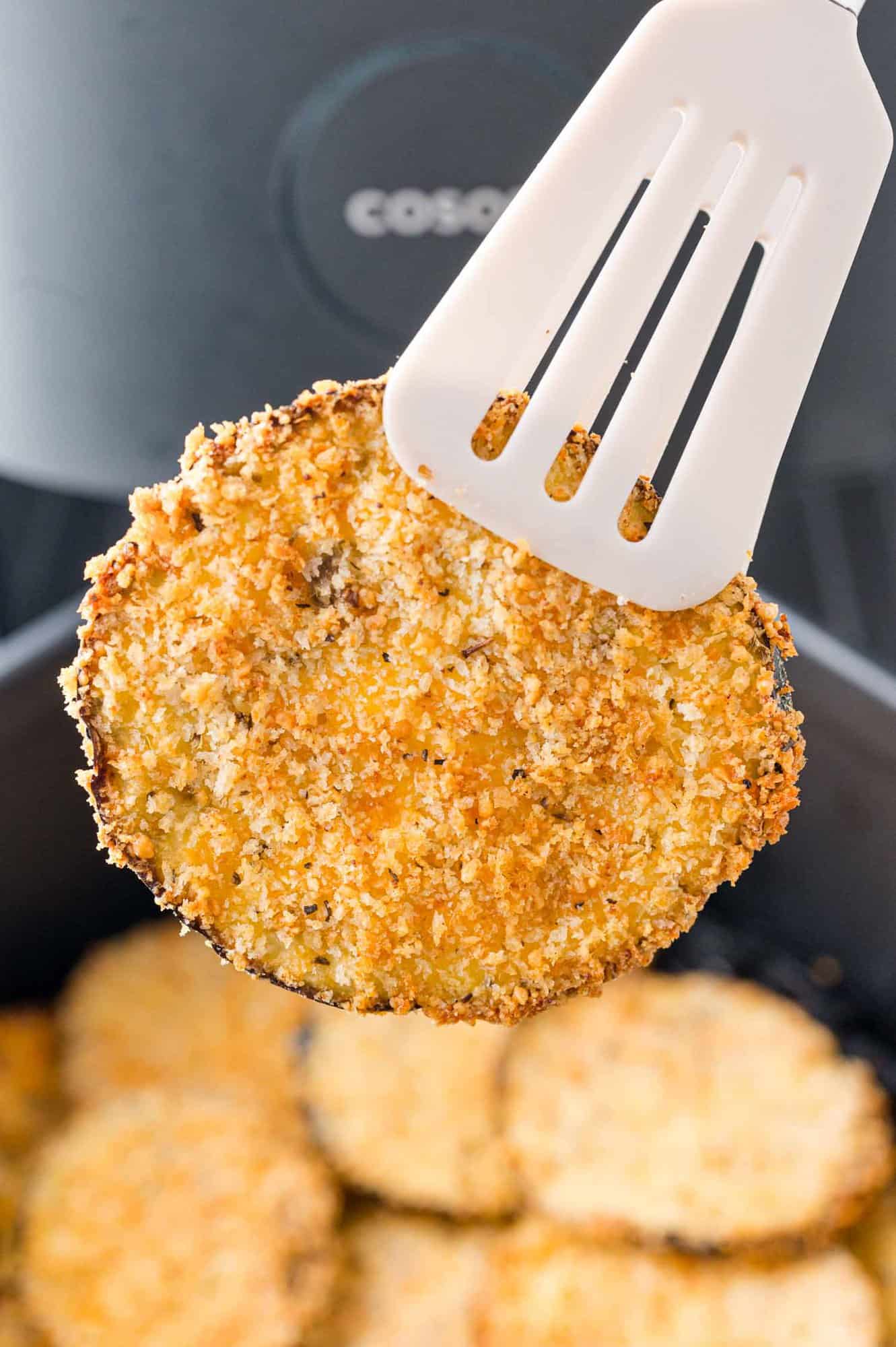Crispy eggplant slice being removed from the air fryer with tongs.