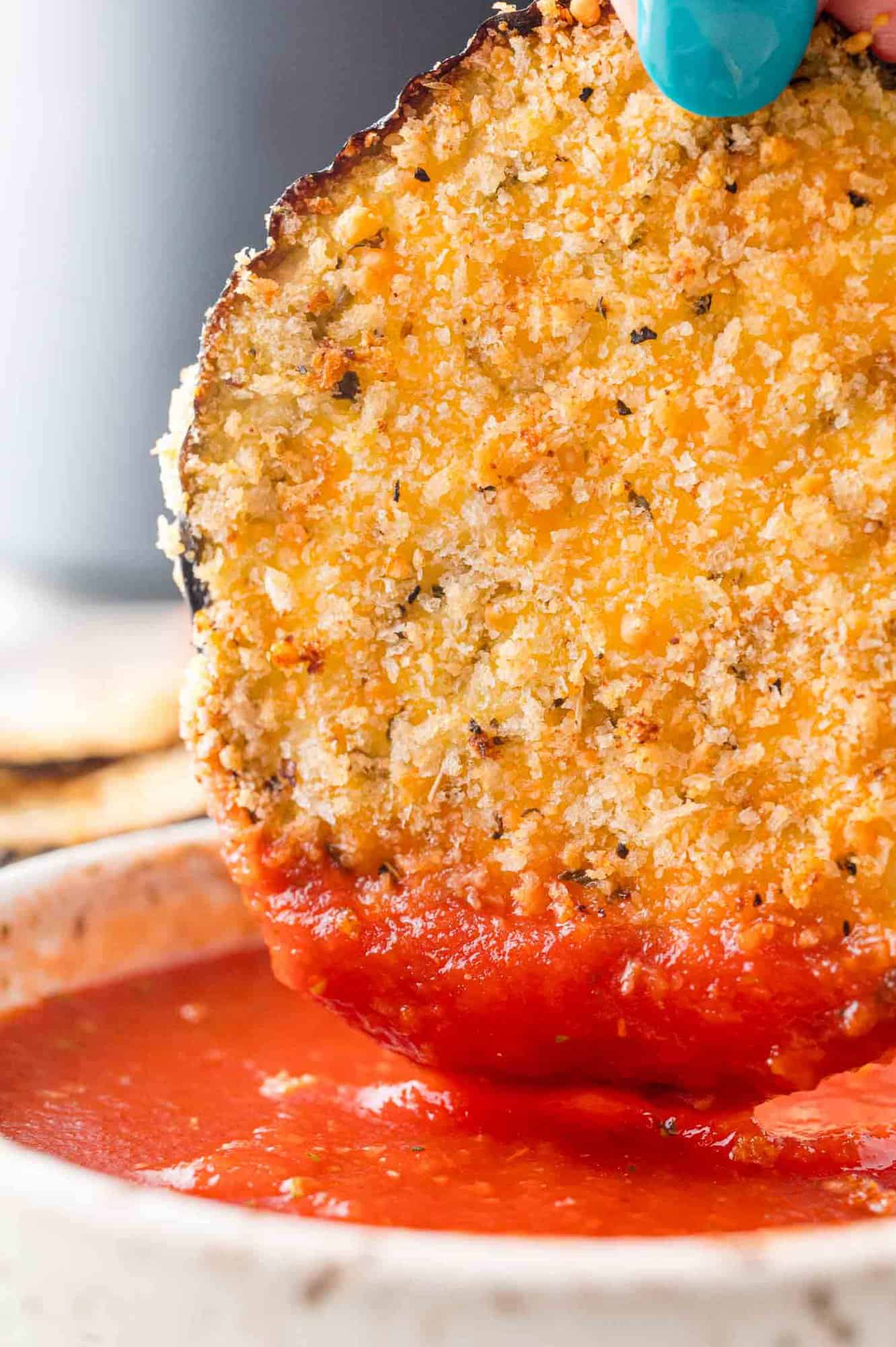 Slice of air fryer eggplant being dipped in marinara sauce.