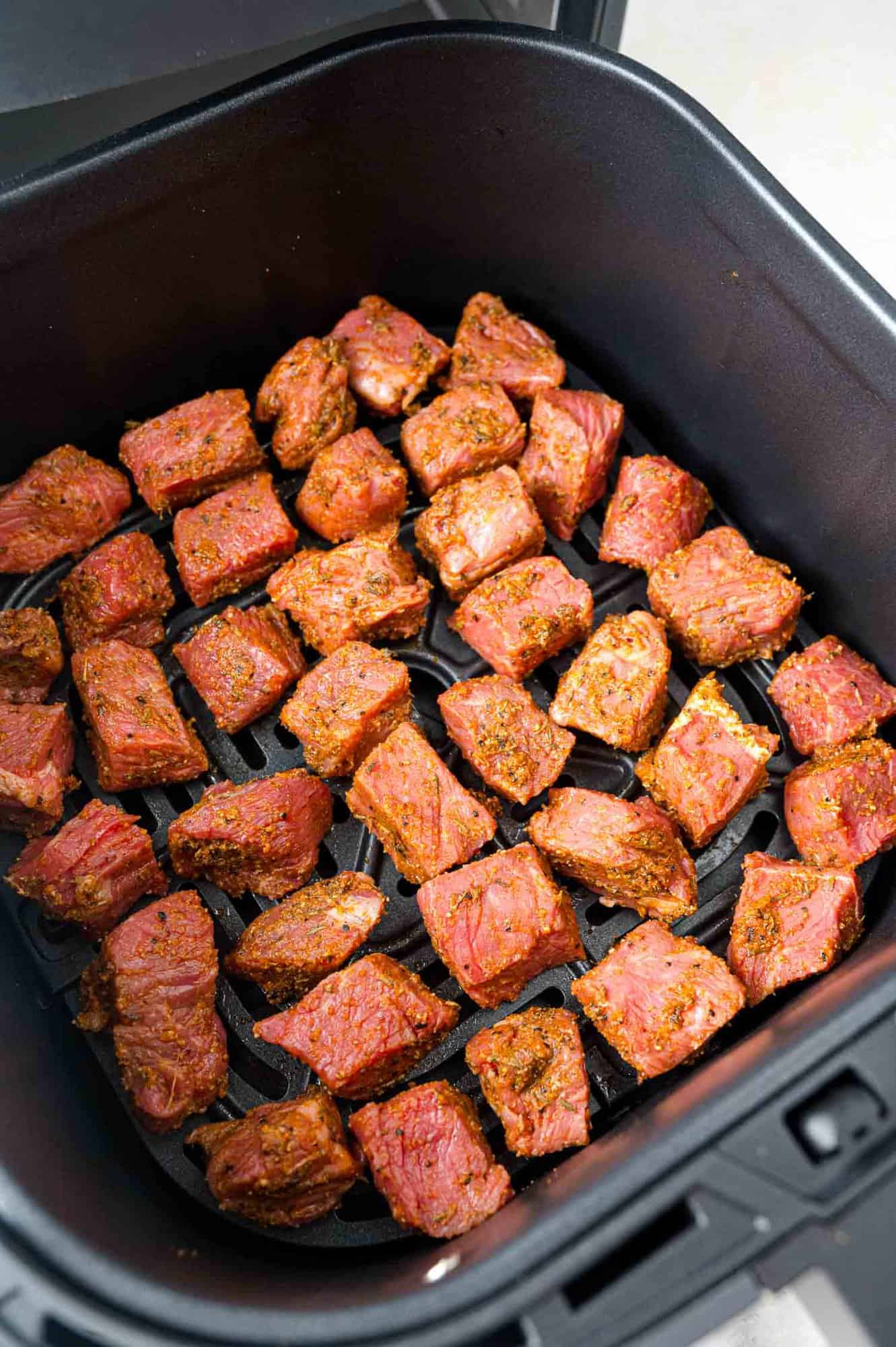 Seasoned steak bites in air fryer, before cooking.