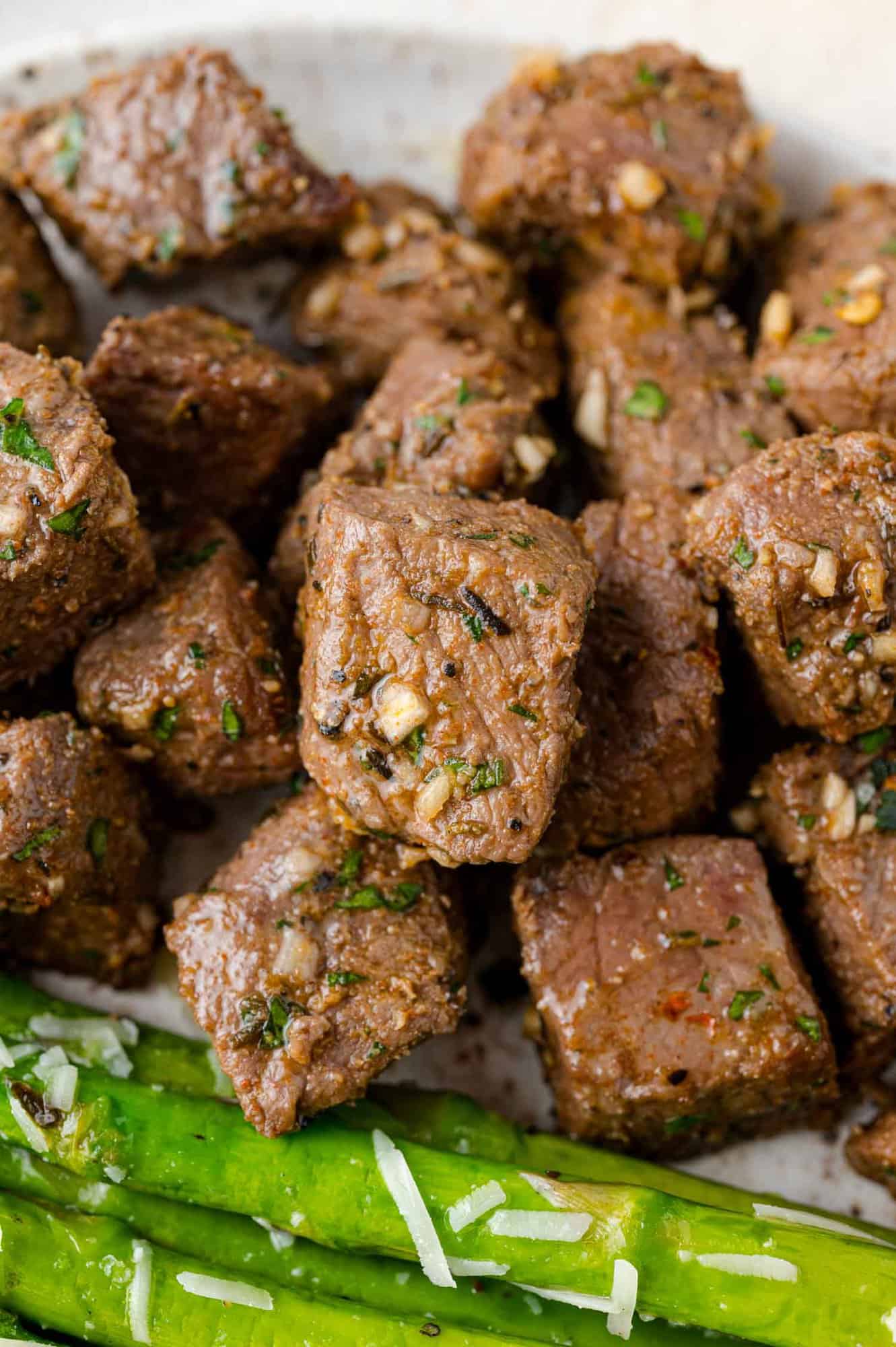 Steak bites on a plate next to sautéed asparagus.