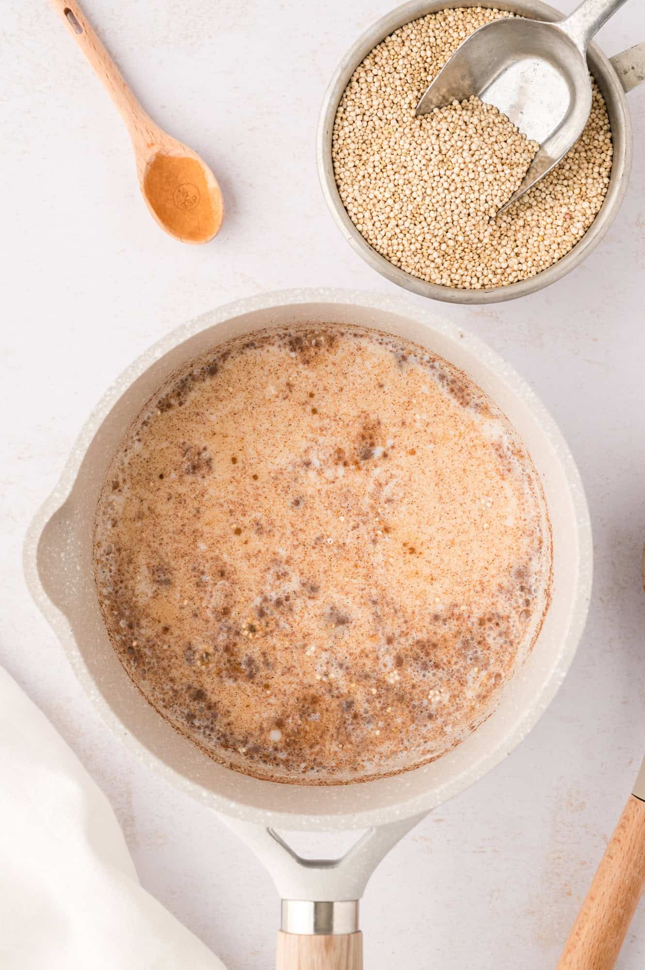 Quinoa and seasonings mixed into the milk, in an off-white saucepan.
