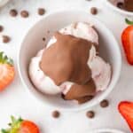 Overhead view of magic shell on top of strawberry ice cream, strawberries scattered around.