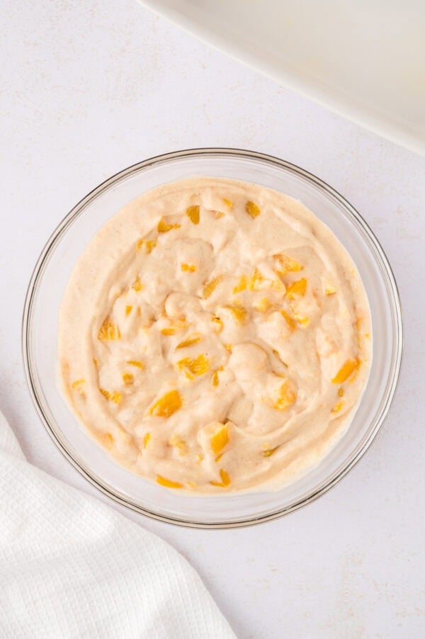 Peach coffee cake batter in a clear glass mixing bowl.