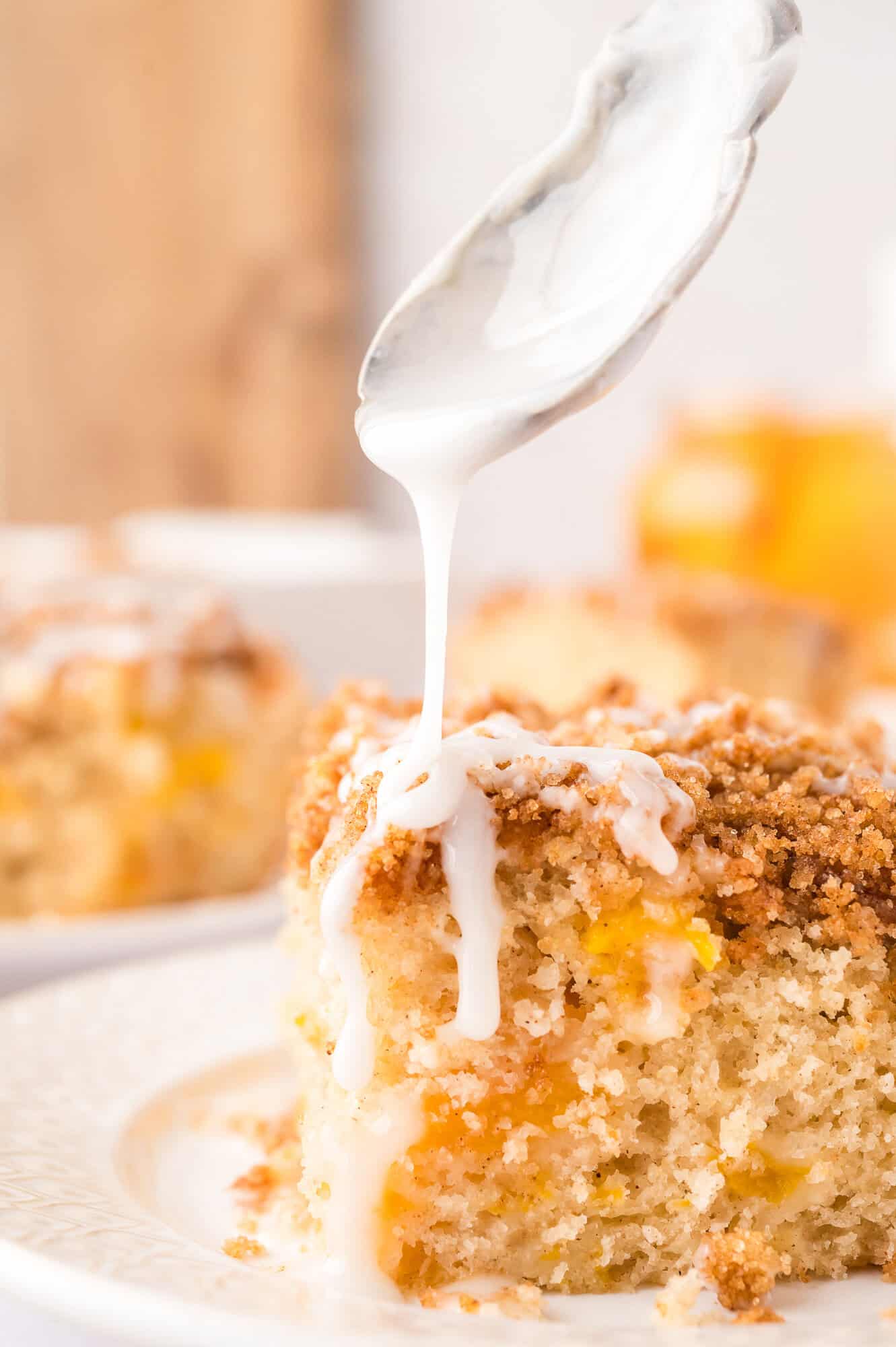 Square slice of peach coffee cake being drizzled with icing.