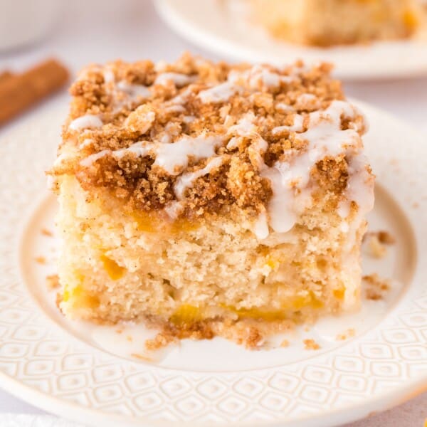 Slice of peach coffee cake on white plate with streusel and icing.