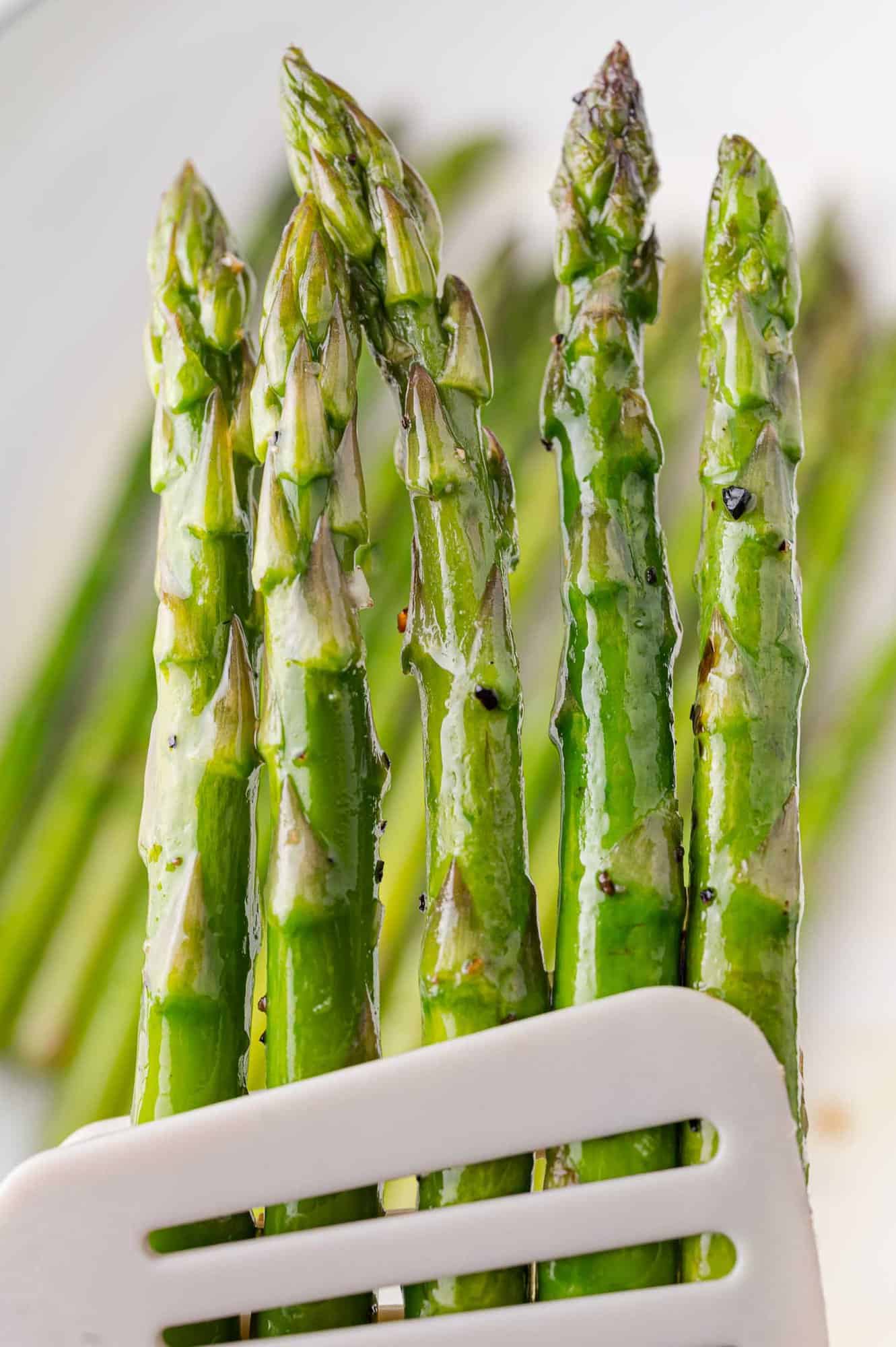 Cooked, crisp green asparagus held with tongs.