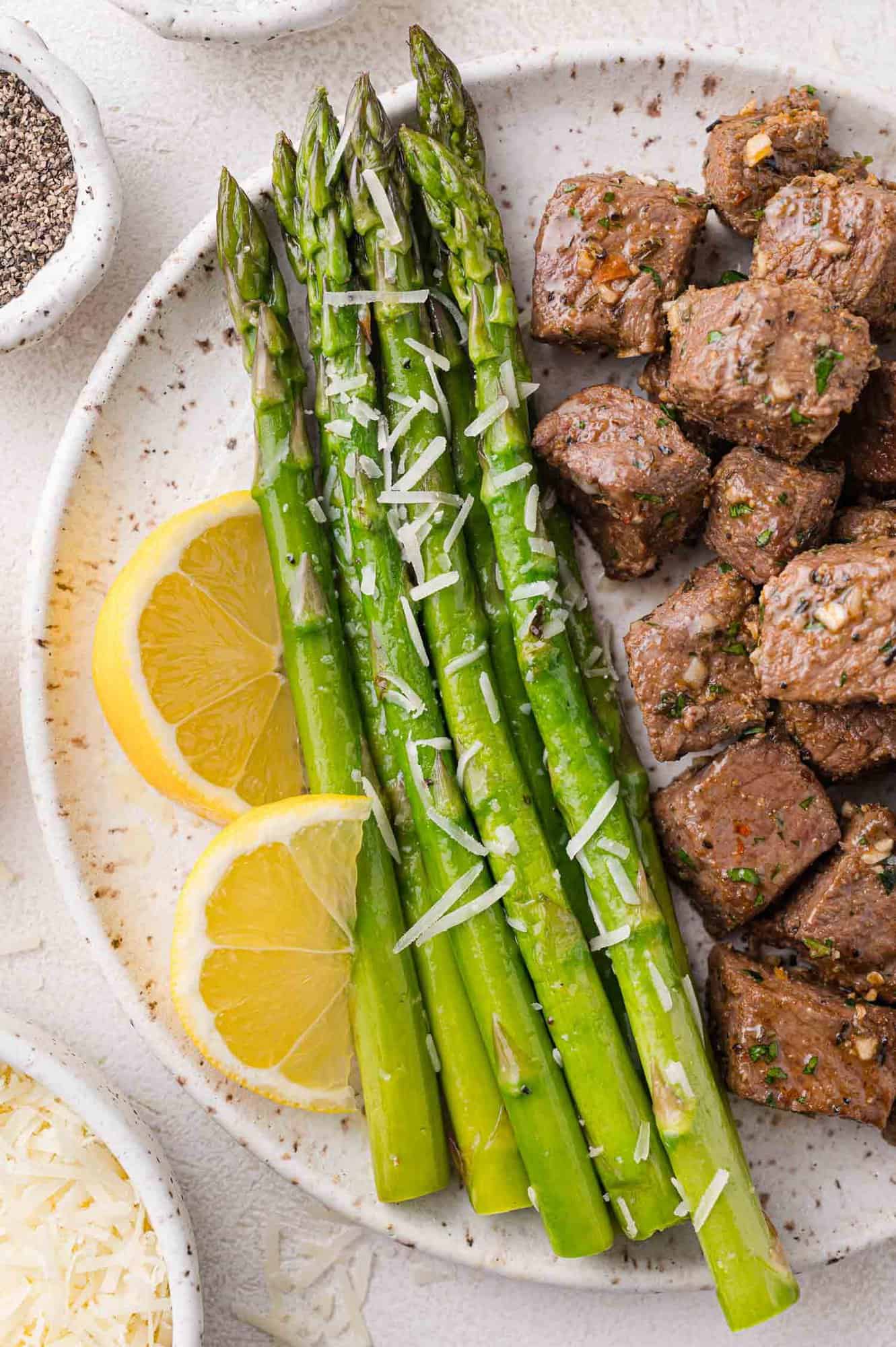 Asparagus on a plate with steak bites and lemon slices.