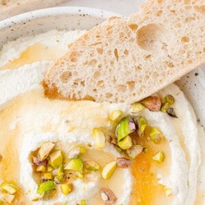 Bread being dipped in whipped feta topped with honey and pistachio.
