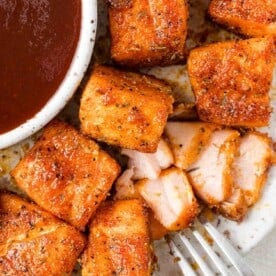 Air fryer salmon bites on a plate, one flaked open to show texture.
