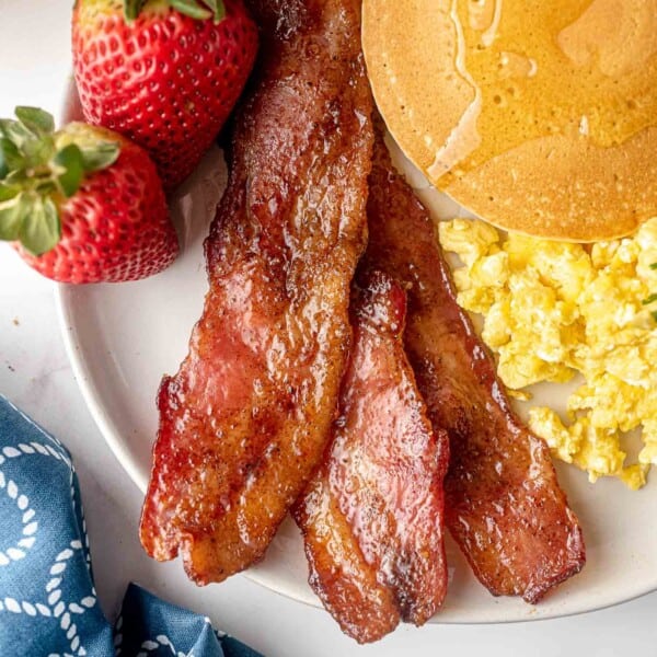 Candied bacon on a plate with pancakes and eggs.