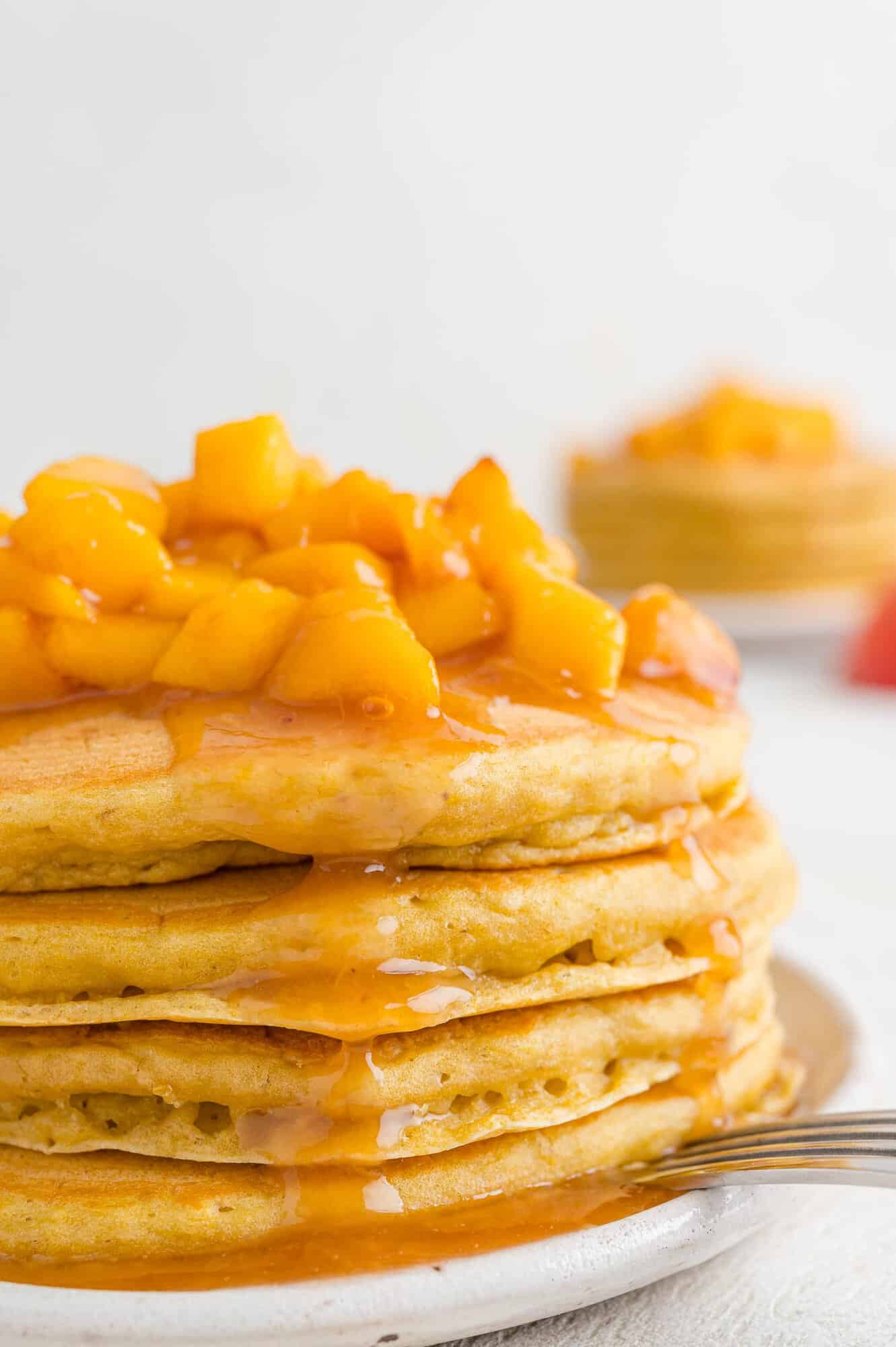 Stack of peach pancakes, topped with peach sauce.