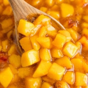 Peach sauce being scooped with a large wooden spoon.