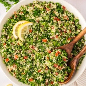 Tabbouleh salad in a large bowl with two wooden serving spoons.