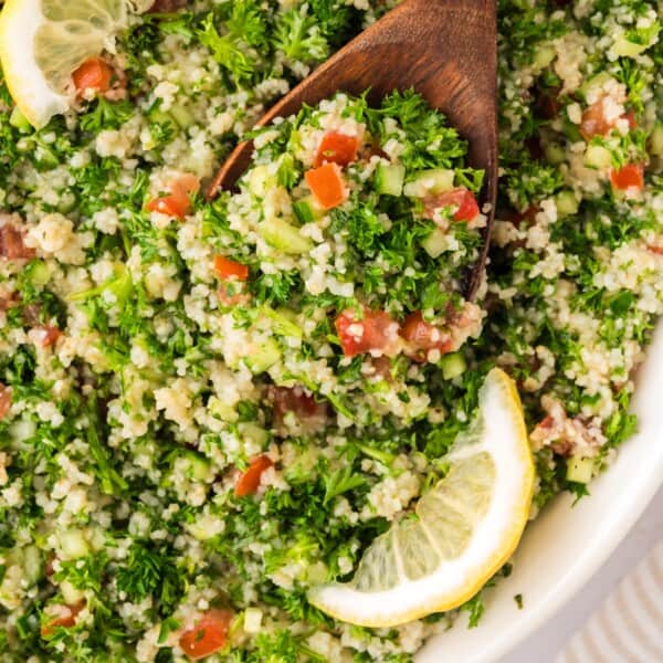 Tabbouleh salad with a large wooden spoon, garnished with lemon slices.