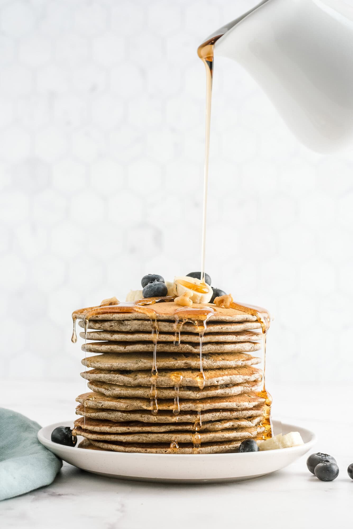 Tall stack of buckwheat pancakes topped with blueberries and maple syrup.