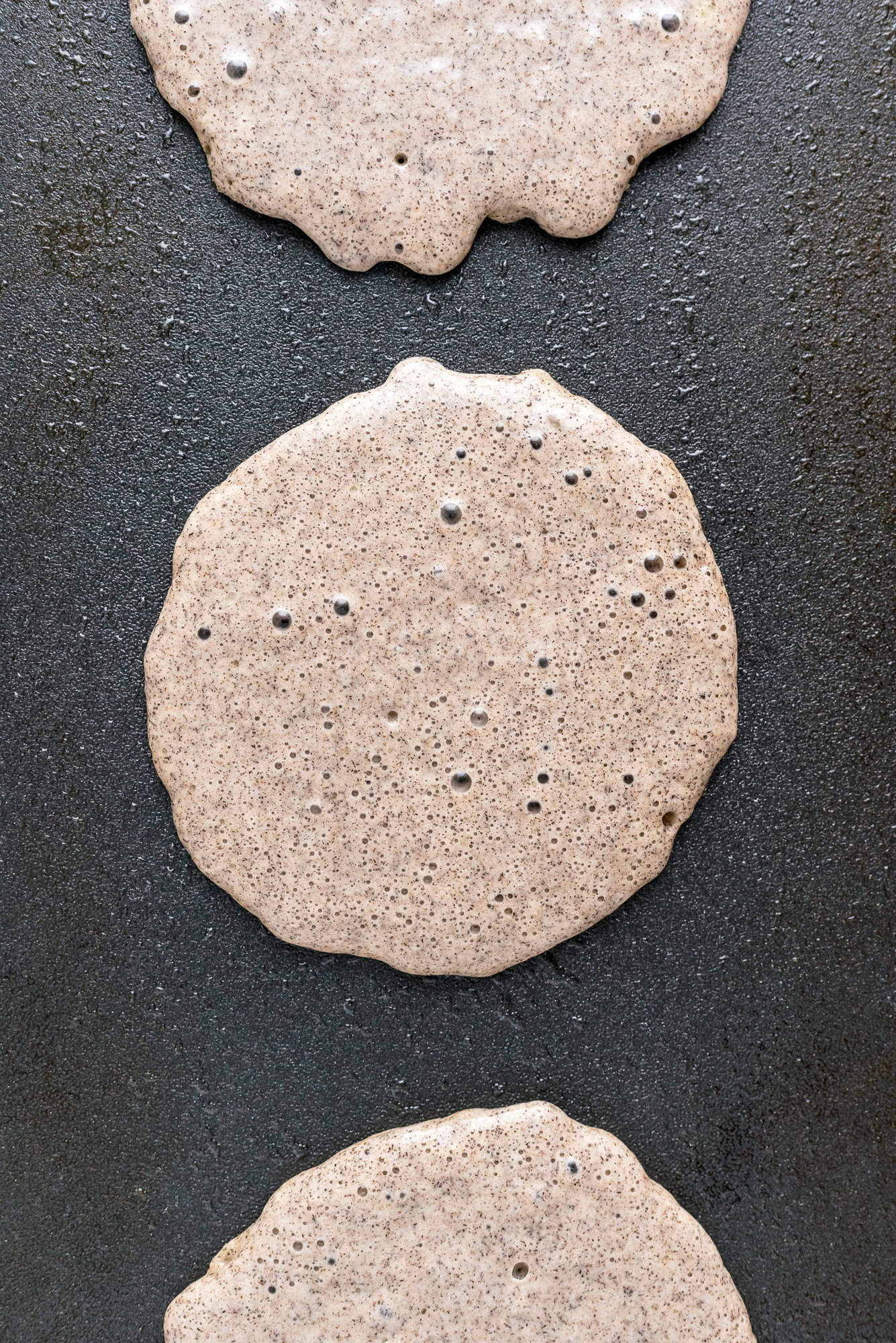 Uncooked buckwheat pancakes on a black griddle.