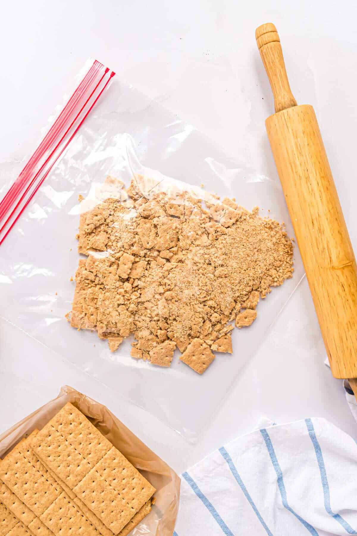 Graham crackers being crushed in a zip-top bag with a wooden rolling pin.