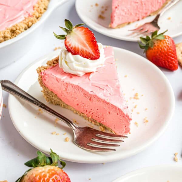 Strawberry Kool Aid pie topped with whipped cream and a half of a strawberry.