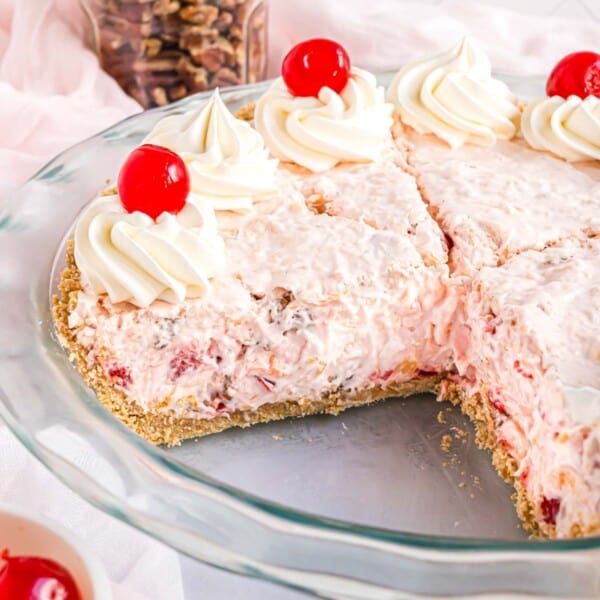Millionaire pie topped with cherries and whipped cream, one slice removed from pie plate.