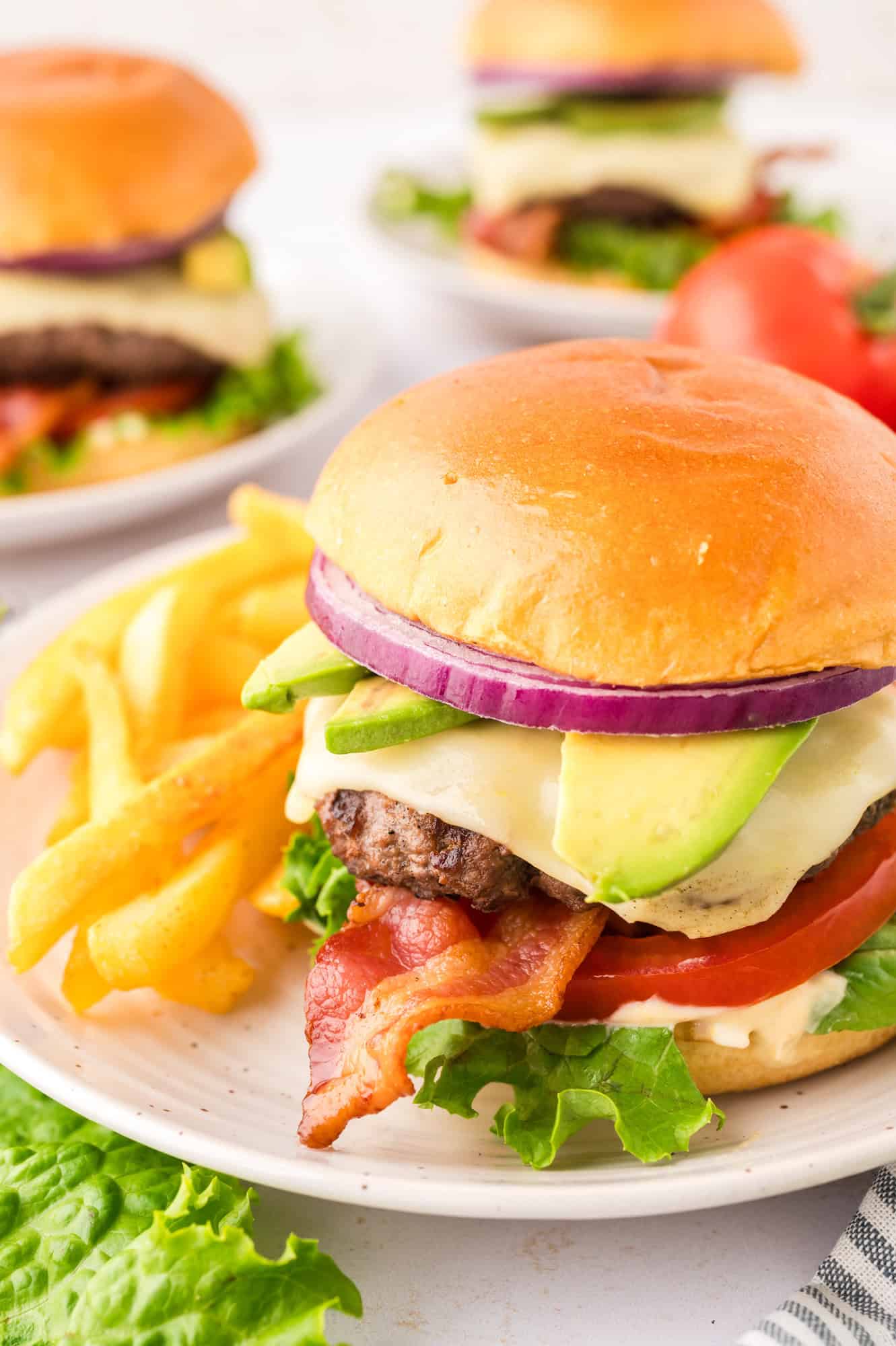 California burger on a plate: brioche bun, beef burger, bacon, lettuce, tomato, onion, sauce.