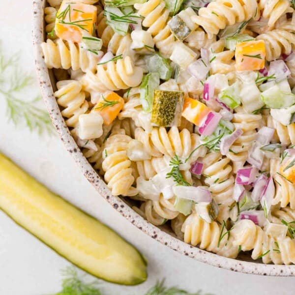 Dill pickle pasta salad with rotini pasta, in a bowl, with a dill pickle next to it.