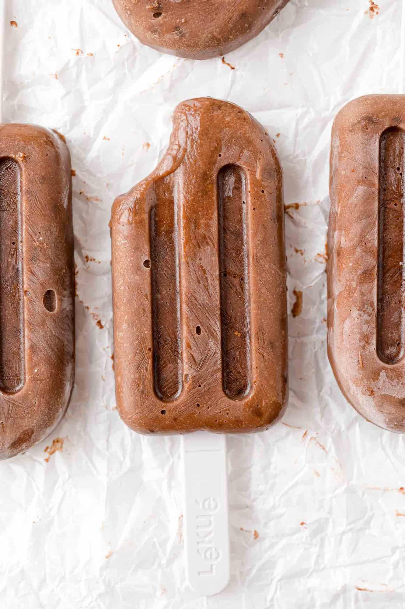Three chocolate pudding pops, one with a bite removed.