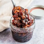 Bacon jam in a small jar, being scooped out with a spoon.