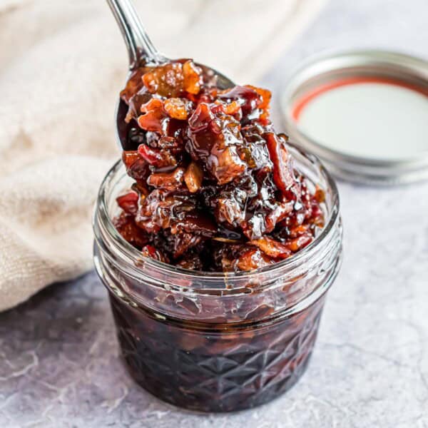 Bacon jam in a small jar, being scooped out with a spoon.